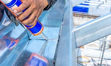 Man Putting Sealant on Metal Surface — Building Supplies in Maitland, NSW